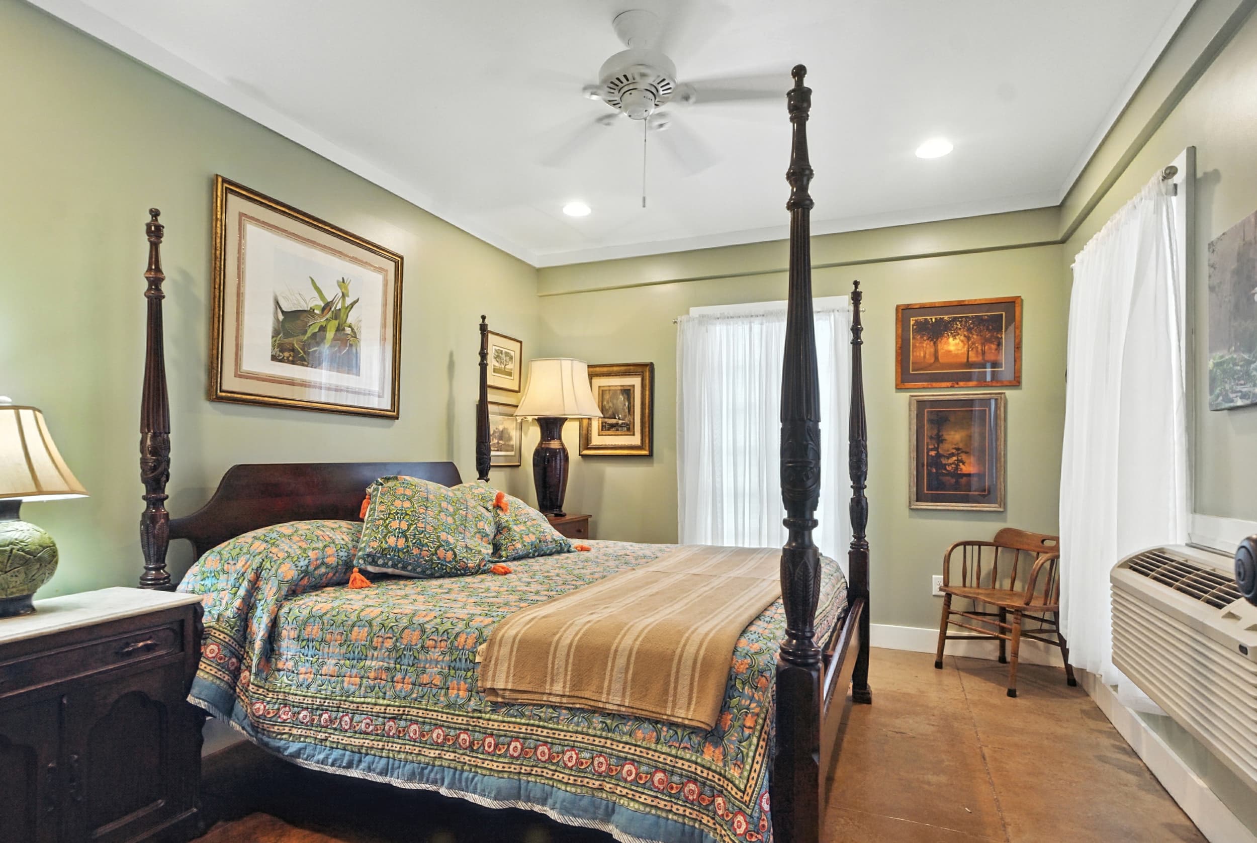 Cozy bedroom featuring sage green walls, a dark wood four-poster bed with a patterned quilt, and rustic hardwood floors.