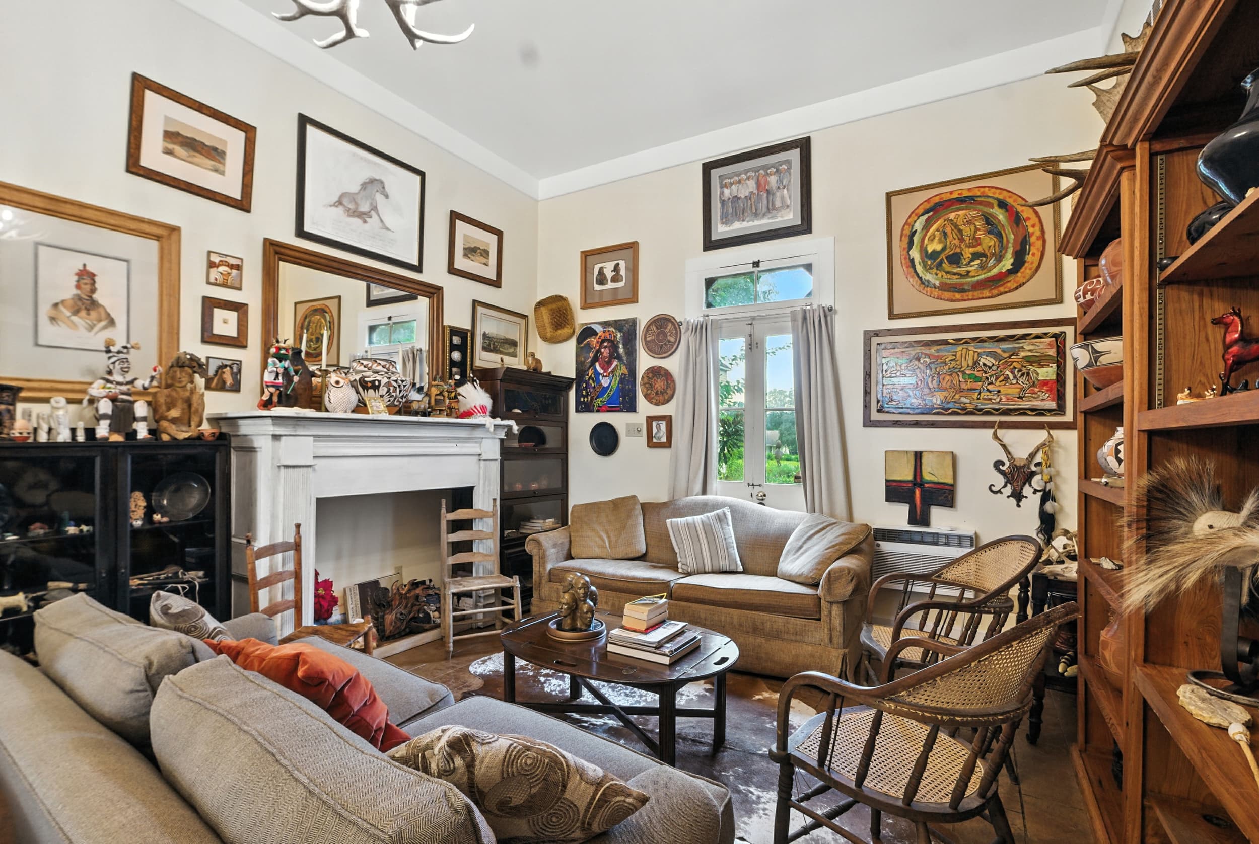 Eclectic living room featuring a floor-to-ceiling gallery wall of art, a white fireplace mantel, cozy sofas, and shelves filled with unique decor.