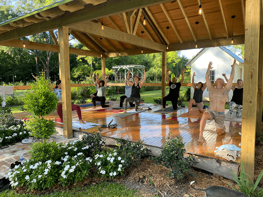 A diverse group of people practicing yoga in a wooden pavilion surrounded by greenery.