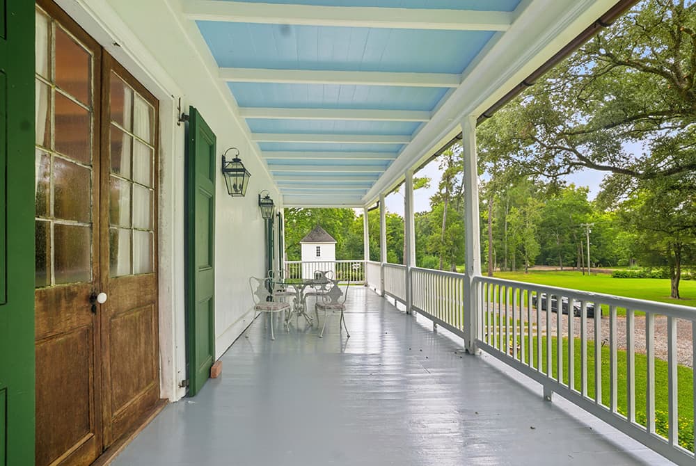 A porch with green doors and white furniture overlooks a grassy yard.